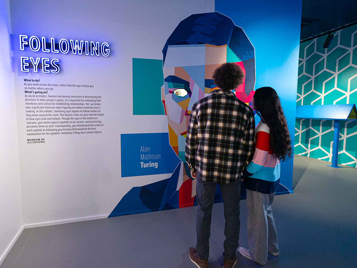 A man and a woman, their backs turned towards the camera, are looking at the Following Eyes exhibit at Museum of Illusions Manchester.