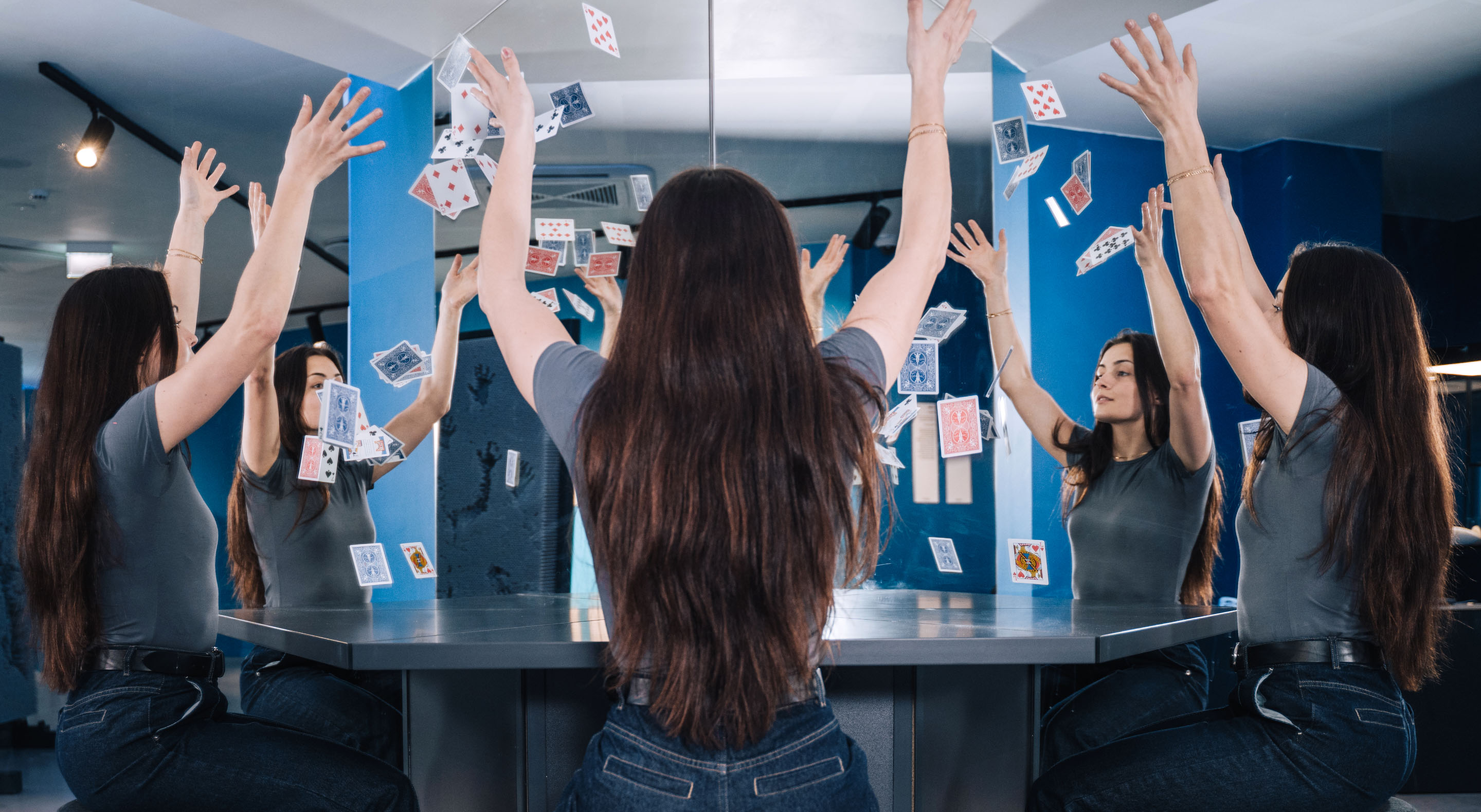 A visitor is throwing playing cards in the air while sitting at the Cloning Table. She appears to be playing with her own reflections.