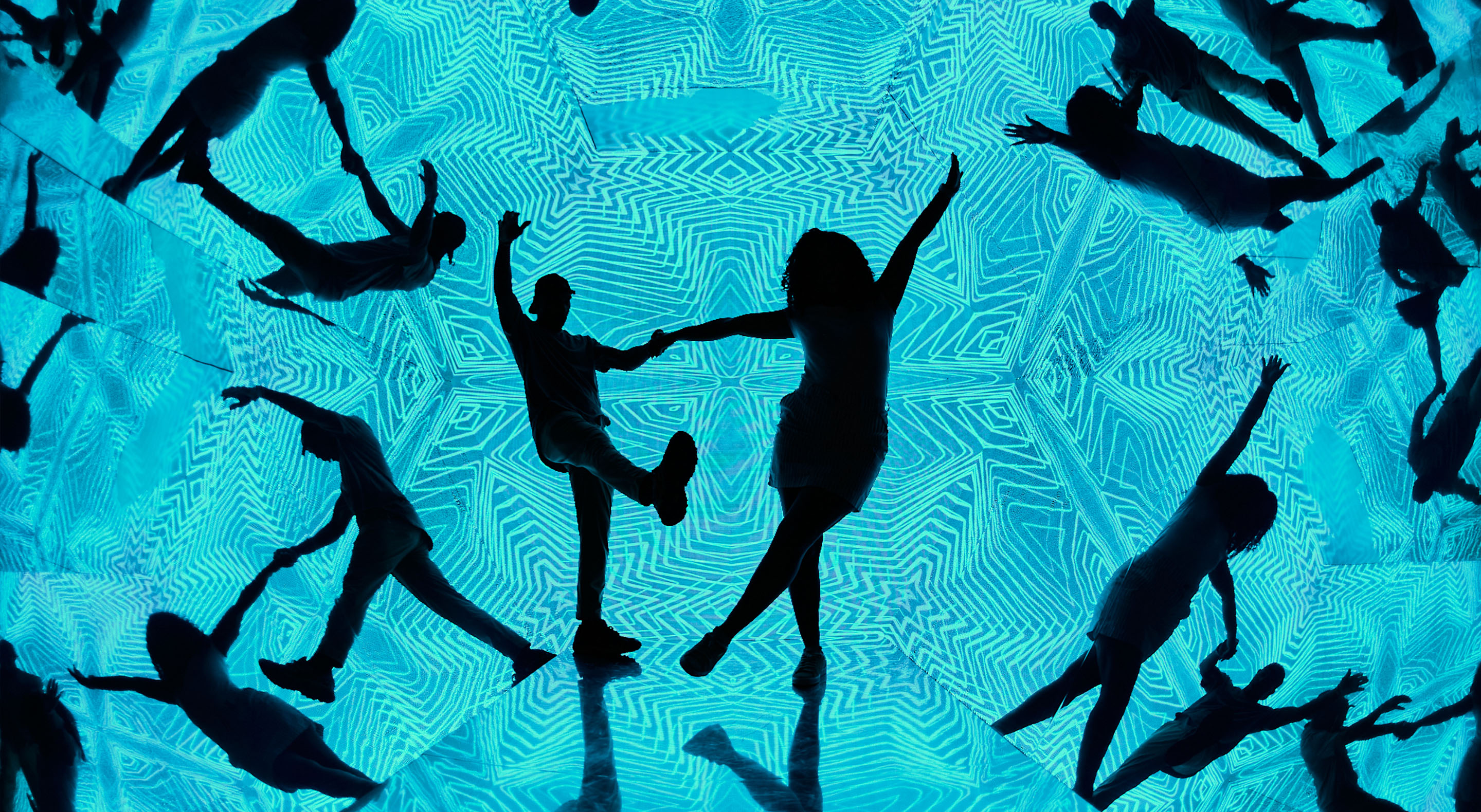 Two visitors dancing in the Walk-in-Kaleidoscope. Their silhouettes are in contrast with the geometric background pattern.