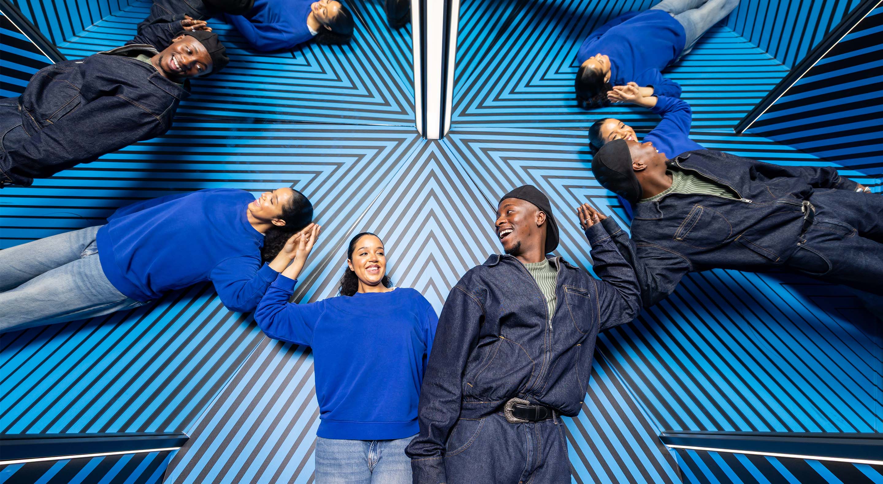 A young couple is smiling while surrounded by their own reflections in the Museum of Illusions' Clone Room.