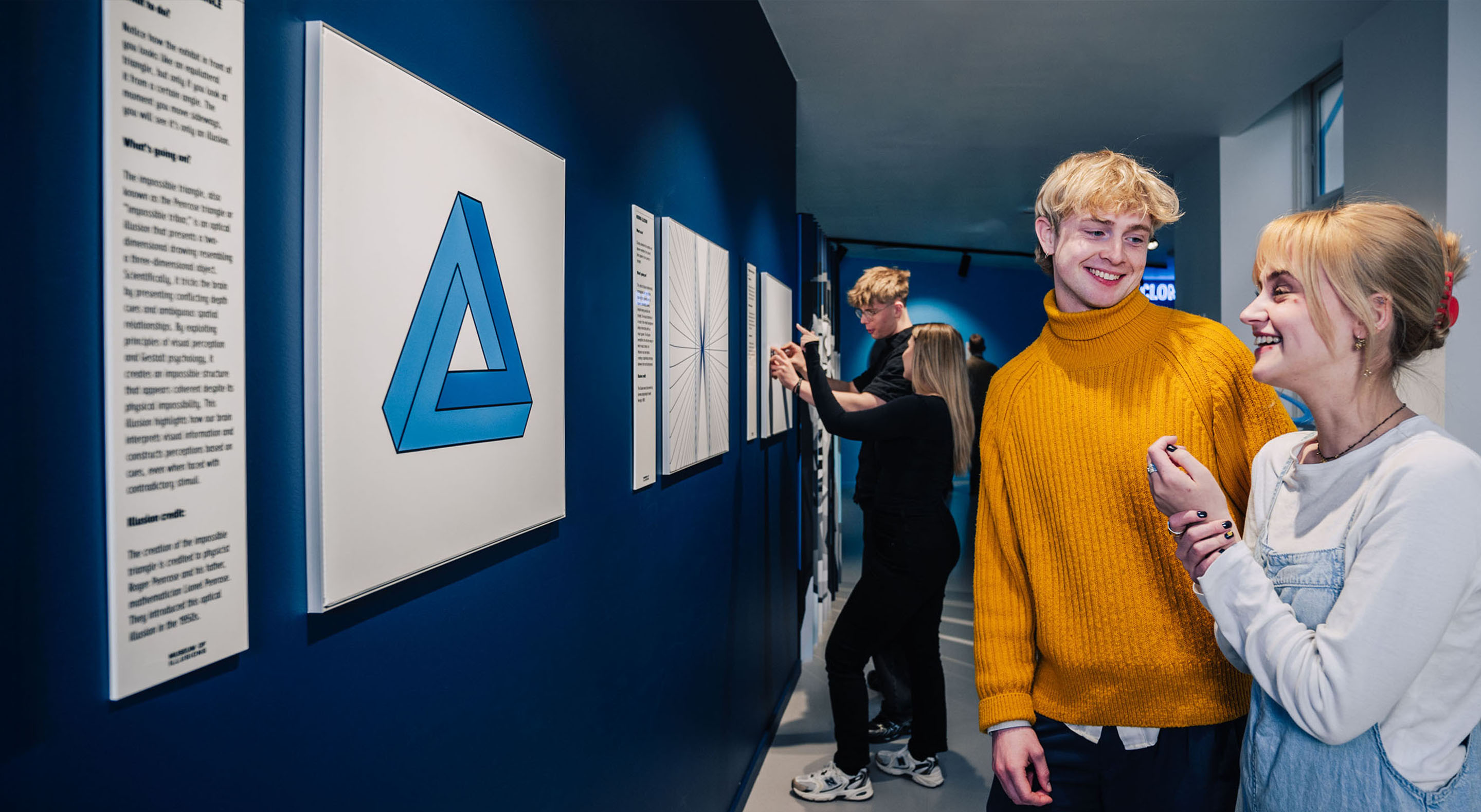 Visitors are looking at the Penrose Triangle illusion displayed on the wall.