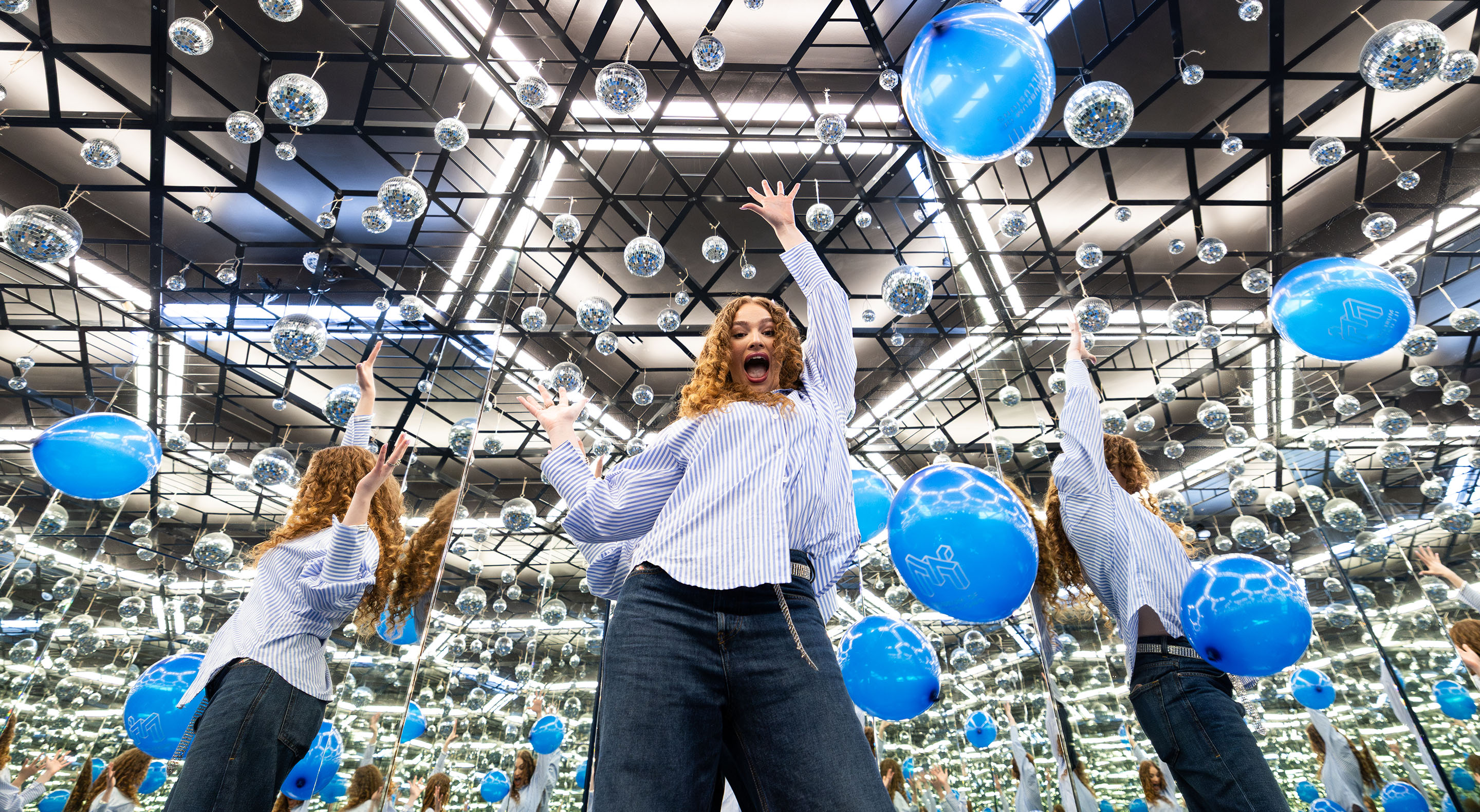 A young person is having fun, hands in the air, in the Infinity Room, surrounded by balloons.